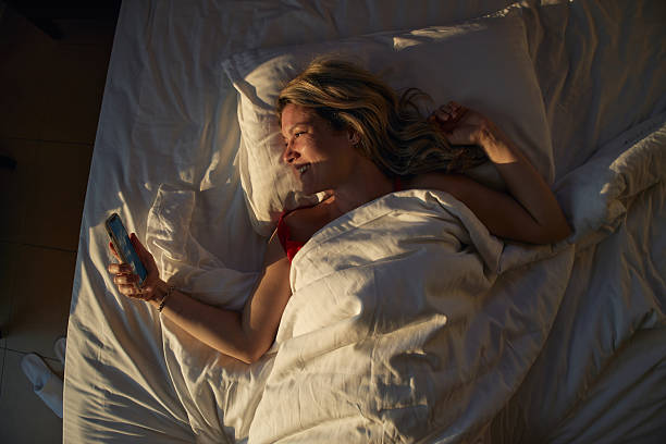 istock Woman relaxing in bed using smartphone in morning sunlight 2236741026