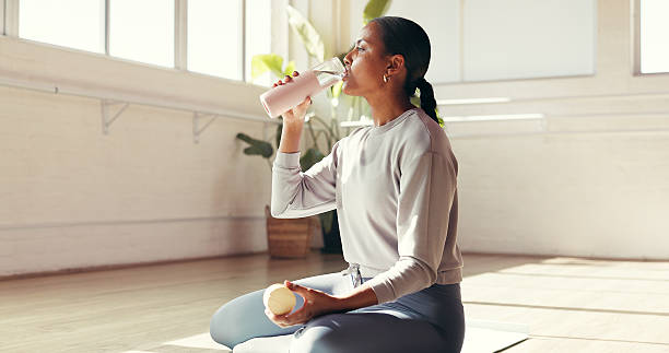 istock Woman, break or drinking with water in studio for hydration, recovery or natural sustainability. Female person, yogi or thirst with mineral liquid or bottle for fitness workout or rest in health club 2236741509