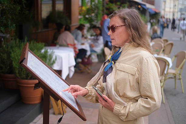 Woman looks at restaurant menu outside. Visitor reads menu on street. Modern dining experience. Middle-aged woman (50 years old)