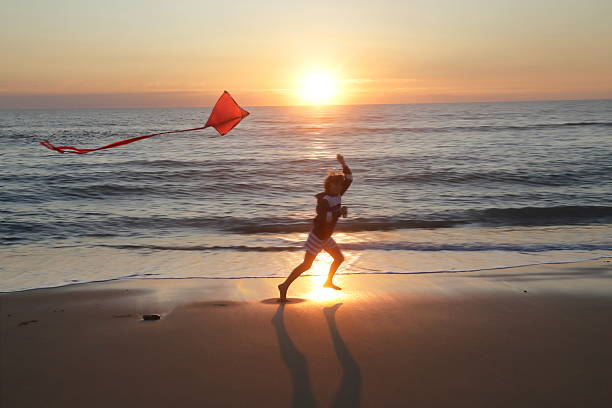Young boy runs on beach with kite at sunset, Soulac, France