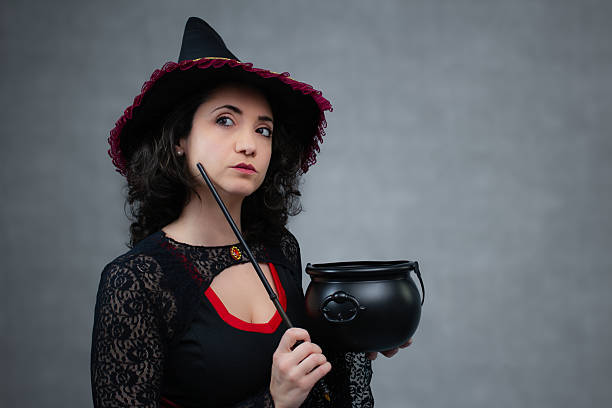 A  silhouetted witch stirs a potion in a cauldron against a backdrop of a rising full moon and a evil sky on Halloween night.