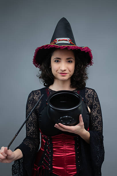 istock Charming mid-adult witch pointing a magic wand at empty cauldron, looking at camera. 2236747342