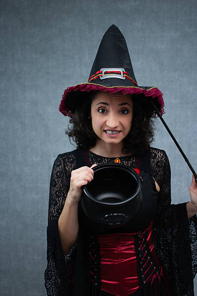 Funny witch holding magic wand and empty cauldron, worried about her potion.