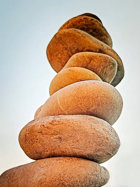 Close-up of a balanced stack of stones on a stone surface, with an old stone chapel blurred in the background. Concept of balance, mindfulness, spirituality, heritage tourism, and peaceful travel destinations.