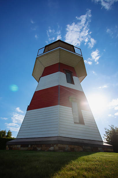 istock Red and white striped lighthouse viewed from below with bright sunlight and blue sky, green grass at the base, creating a dramatic coastal architecture scene. 2236753927