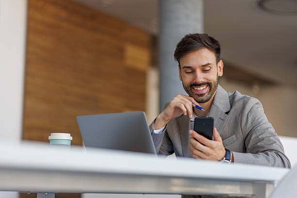 istock Young businessman smiling at smartphone while working at modern office desk 2236754001