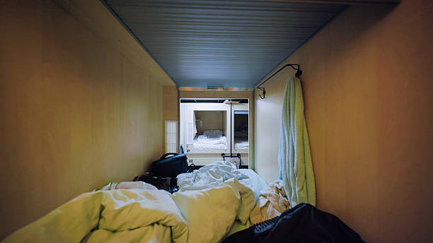 Interior of a small capsule hotel room with personal belongings and unmade bed