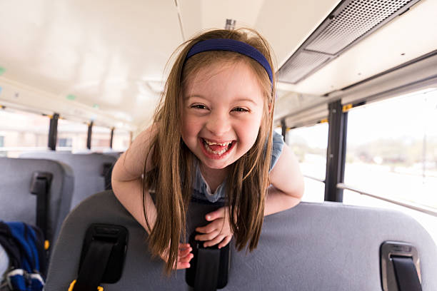 Two young children smile as they pop up from their seats on a school bus.  They are both dressed casually and are smiling as they ride home after a long day pf school.