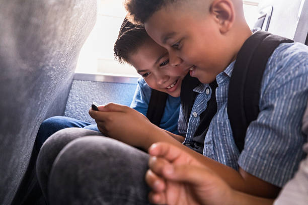 Elementary school boys enjoy using a smartphone together on a school bus.