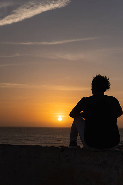 istock Person silhouette sitting watching sunset over ocean horizon 2236758235