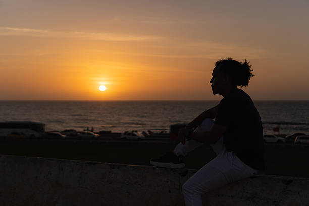 Man silhouetted against a golden sunset over the ocean, sitting and contemplating