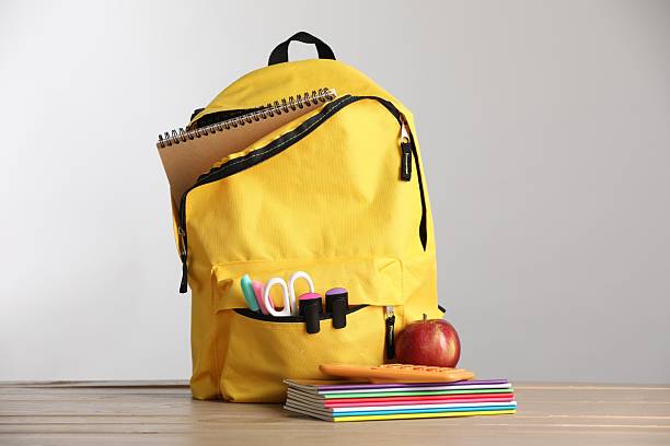 istock Yellow backpack, stationery and red apple on wooden table against light grey background 2236759457