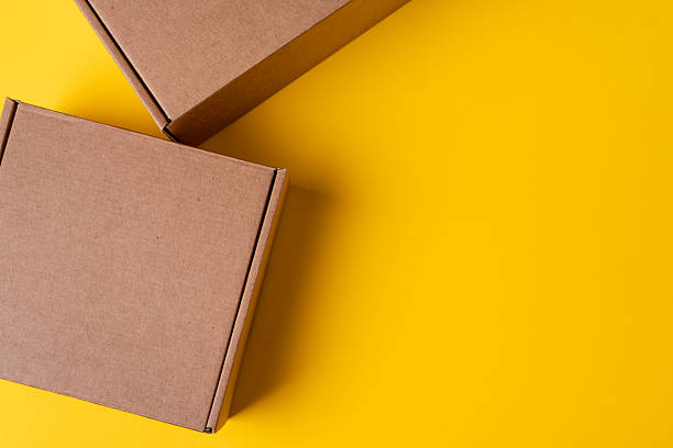 istock Beige cardboard boxes on yellow background, close up 2236759876