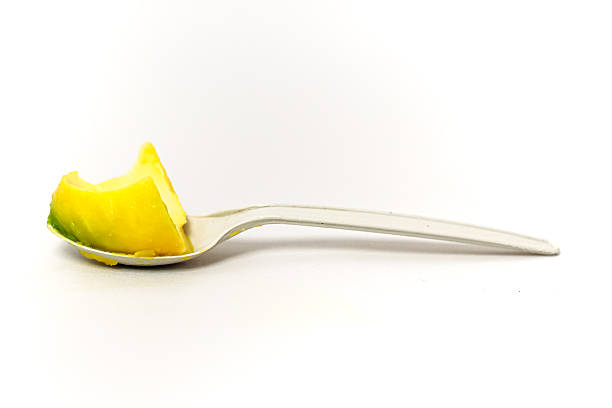 A slice of ripe mango served on a disposable plastic spoon against a white background.