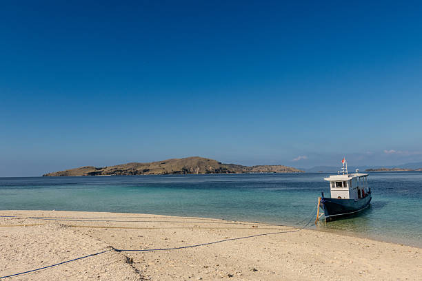 Traditional boat resting on a sandy tropical beach in Indonesia, with calm turquoise water and clear sky in the background