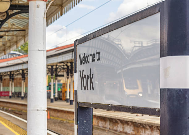 York, UK. August 26, 2025.  A railway station welcome sign with a reflection of a locomotive and arches.  A historic 19th Century canopy supported by a column is above.