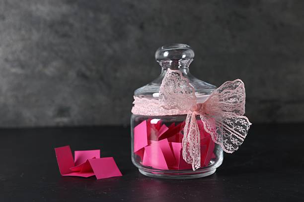 istock Pink paper notes in glass jar with ribbon on black table 2236763903