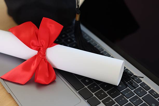 istock Open laptop and rolled diploma with red bow on wooden table, closeup 2236764244