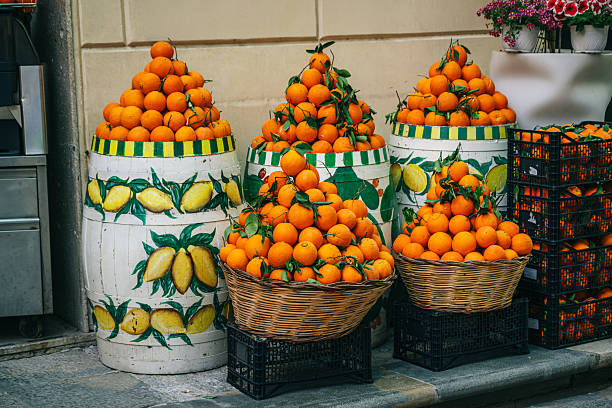 istock Oranges Piled in Baskets Beside Lemon-Patterned Barrels at a Sicilian Street Market 2236764857