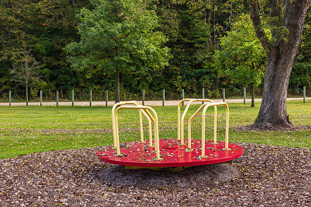 A red and yellow merry go round in a park by the woods during early autumn.