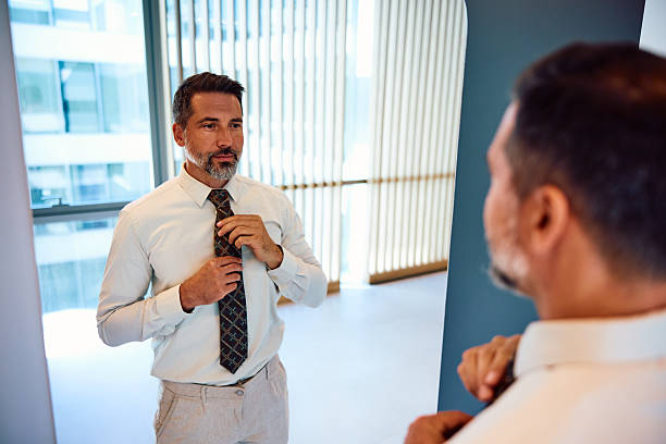 istock Mid adult man adjusting tie in mirror before work 2236766326