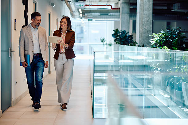 istock Two mid adult colleagues walking and discussing work in modern office hallway 2236766810