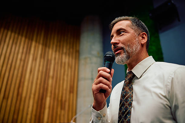 Mature adult businessman speaking into a microphone, delivering a corporate presentation with a world map on screen
