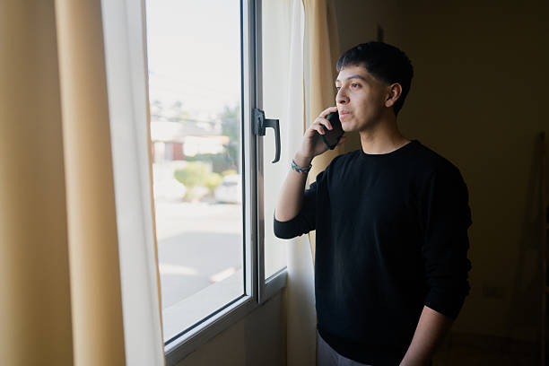 istock Young adult man talking on phone while looking thoughtfully out window 2236767802