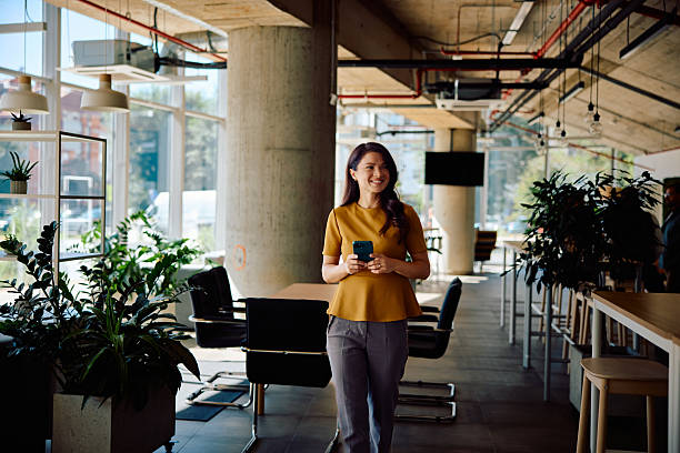 istock Confident young adult woman smiling with smartphone inside modern office workspace 2236767890