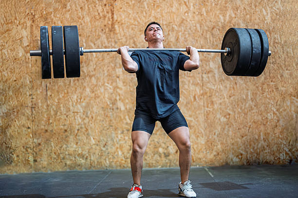 An athlete lifts a heavy barbell overhead with determined focus in a modern gym setting during a training session.