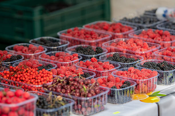 Assortment of fresh berries in plastic containers at a market stall. Raspberries, blackberries, and currants on display, symbolizing organic farming, healthy nutrition, and summer harvest