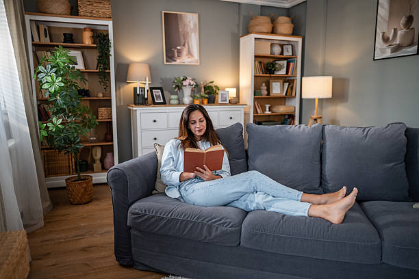 istock Relaxed young woman reading book on cozy grey sofa 2236780887