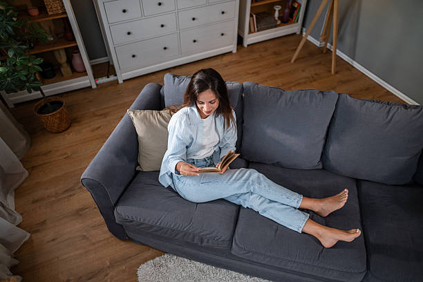 istock Relaxed young woman reading book at home on cozy gray sofa 2236780965