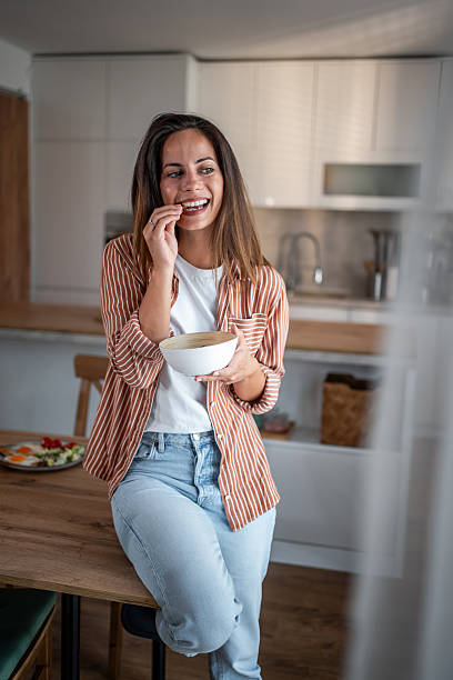 istock Smiling young woman eating snack in modern kitchen 2236782117