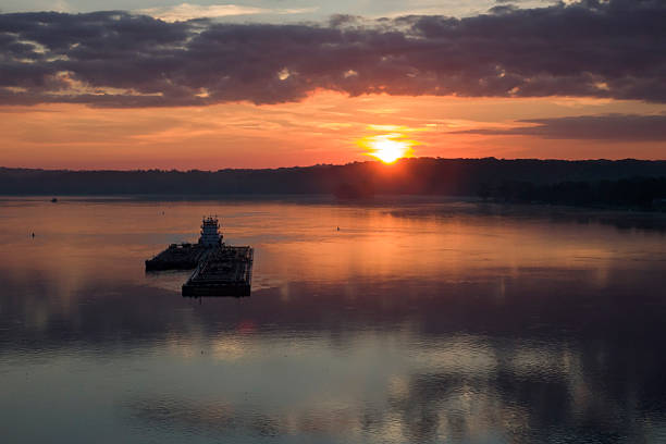 As the sun crests the tree line, bright reflections shimmer in the morning sun as a barge transporting goods passes by in the Mississippi River on the Iowa and Illinois border at Moline, Illinois.