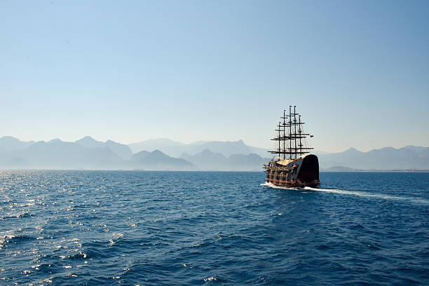 Sailing a traditional ship across calm waters near a scenic mountain range in daylight