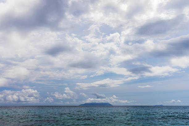 Serene seascape featuring calm waters, a distant island beneath a blue sky with fluffy clouds, evoking tranquility and relaxation. Perfect for travel, nature, and seaside concepts