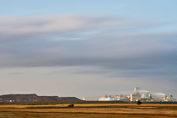 Wide view of an industrial plant facility with storage domes and processing towers in the middle of the Canadian prairies. The scene highlights the contrast between agriculture and heavy industry.