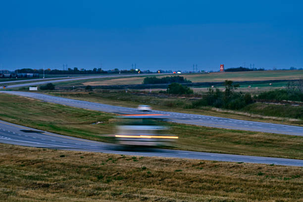 Cars driving along a multi-lane urban highway during early evening. Motion blur suggests movement and daily commuting. Image represents transportation, rush hour, and city mobility.