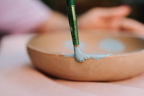 Creative pottery painting captures process of adding blue paint to a handmade clay bowl. Painting a clay bowl with light blue paint. Artisan carefully applies soft blue paint to the rim of clay bowl.