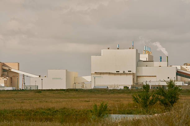 Main processing building of a potash plant in Saskatchewan, Canada, with white industrial architecture, ventilation stacks, and smoke rising under dramatic dark clouds.