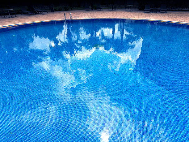 istock Swimming pool water surface with reflected palm trees and clouds 2236808952