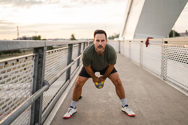 Fit man performing an outdoor workout with a kettle bell on a modern pedestrian bridge, focusing on strength and physical fitness during an urban exercise session