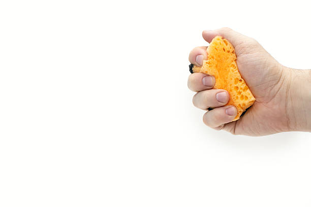 Orange sponge for washing dishes in a hand on a white background. A man's hand squeezes a sponge for washing or cleaning. Free space for text. The concept of cleanliness and housekeeping