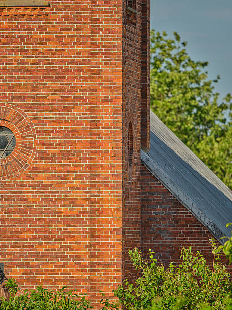 A beautiful historic brick structure is surrounded by vibrant trees and bushes, capturing the peaceful essence of summer in Denmark. The intricate brickwork and tranquil nature evoke feelings of timeless charm.