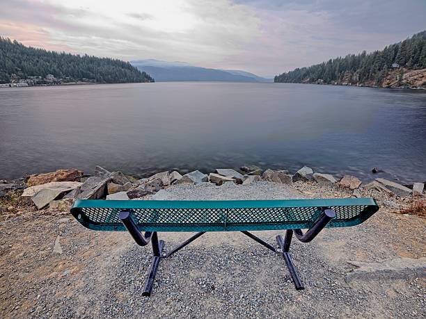 An empty metal park bench on a path of land by Garfield Bay in Pend Oreille Lake in north Idaho.