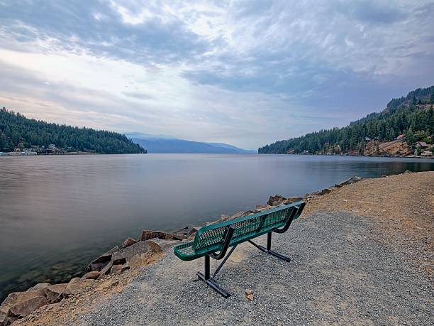 An empty metal park bench on a path of land by Garfield Bay in Pend Oreille Lake in north Idaho.