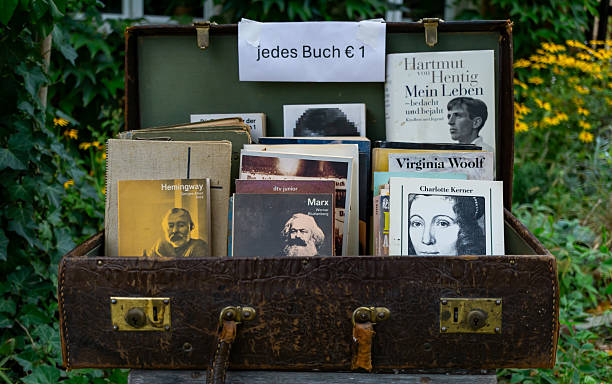 Editorial stock photo of a vintage leather trunk filled with classic literature books, displayed on the side of a street. A handwritten sign reads \