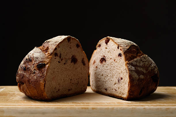 Freshly baked sourdough bread sliced in half on a brown wooden cutting board on a black background