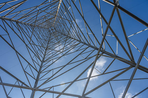 A Low-Angle View of the Structural Framework of a High-Voltage Power Transmission Tower Against a Clear Blue Sky